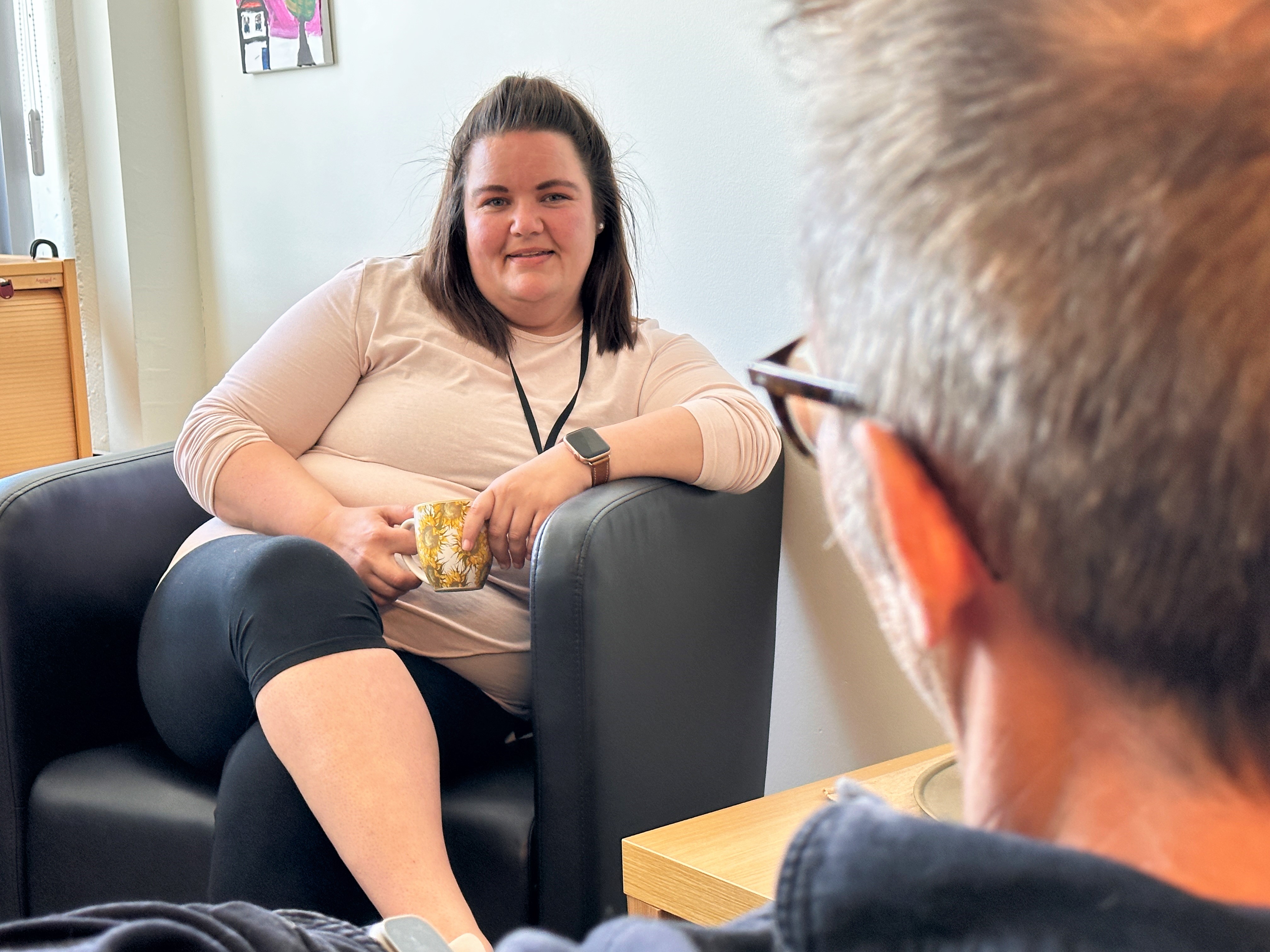 Bildet viser Heidi som sitter i en stol på kontoret sitt. Hun snakker med en person som vi ikke ser ansiktet til.